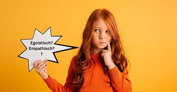 Mädchen mit langen, roten Haaren und einem orangefarbenen Pullover steht vor einem gelben Hintergrund, schaut überlegend und hält eine Sprechblase in der Hand auf der "egoistisch" und "empathisch" steht.