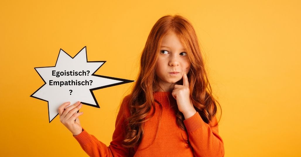 Mädchen mit langen, roten Haaren und einem orangefarbenen Pullover steht vor einem gelben Hintergrund, schaut überlegend und hält eine Sprechblase in der Hand auf der "egoistisch" und "empathisch" steht.